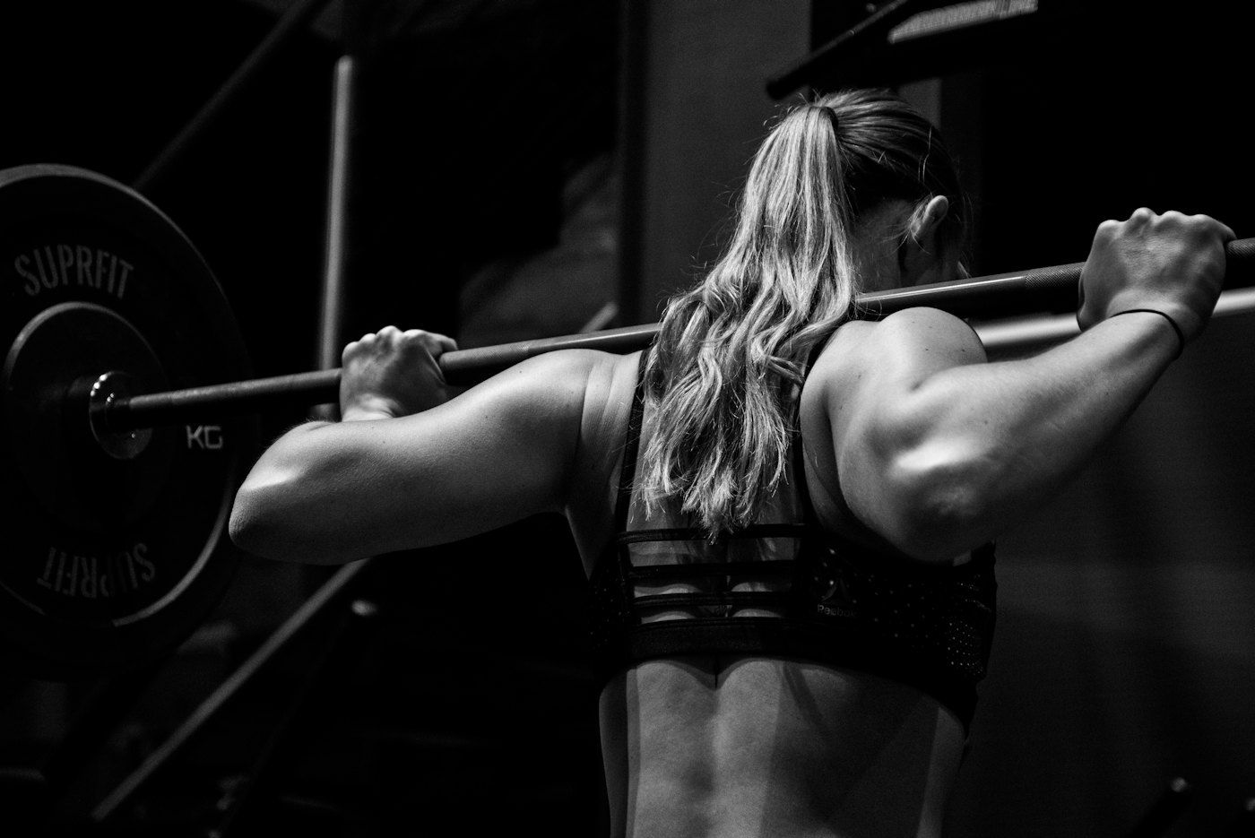Black-and-white photo of an athlete, seen from behind, holding a barbell across her shoulders